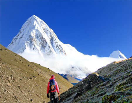 a female trekker close to the everest base camp with gear, mt. pumori and blue sky in a clear day in october.