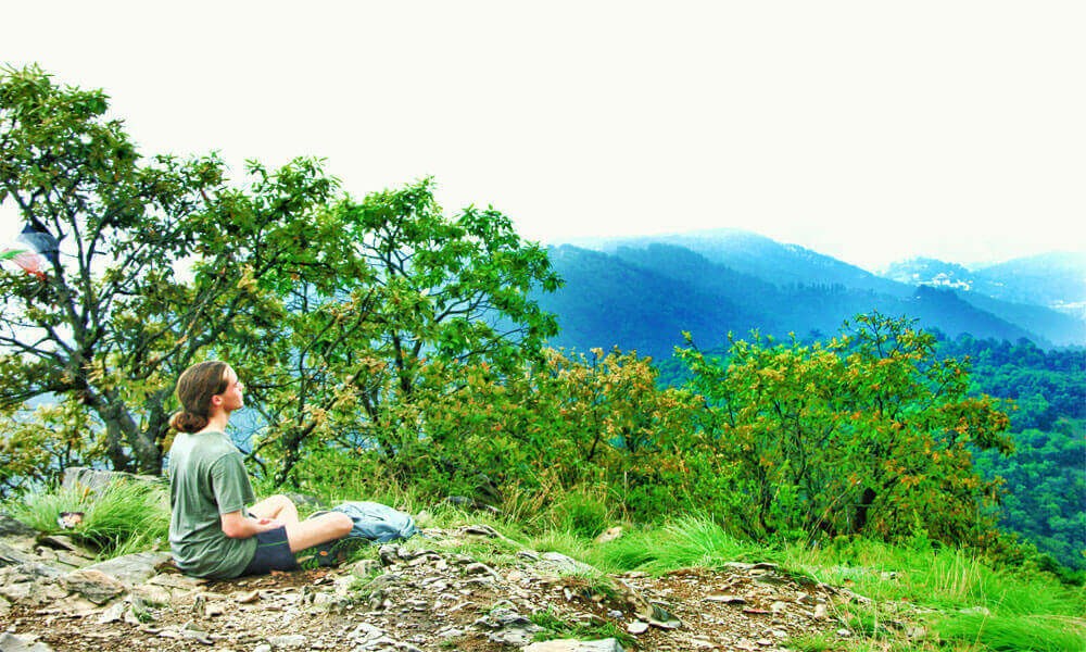 a hiker meditating on the side of champadevi hiking trail, green trees around