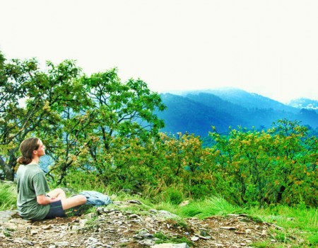 a hiker meditating on the side of champadevi hiking trail, green trees around