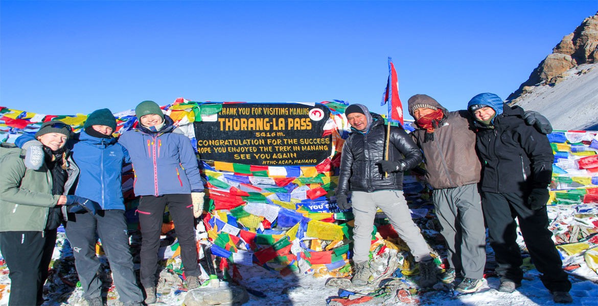 trekkers are at thorong la pass, buddhist prayer flags, and blue sky on a clear day during completing long annapurna circuit trekking distance.