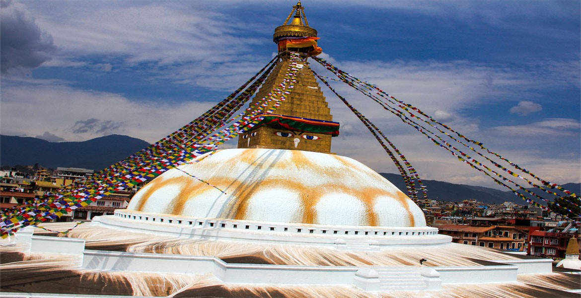 bouddhanath stupa with buddhist prayer flags and green hill views.