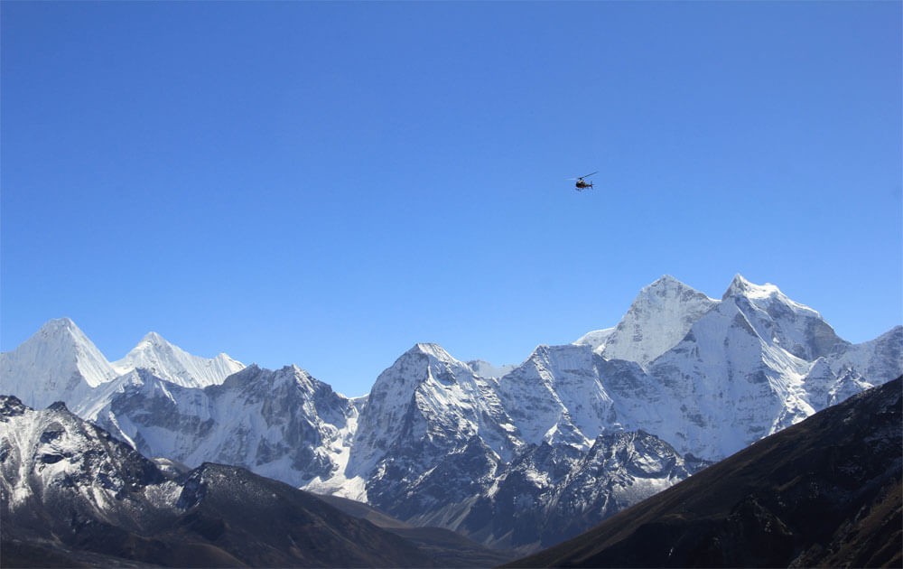 a helicopter is flying above magnificent high mountains in the everest region and the blue sky on a clear day during the everest base camp helicopter tour.