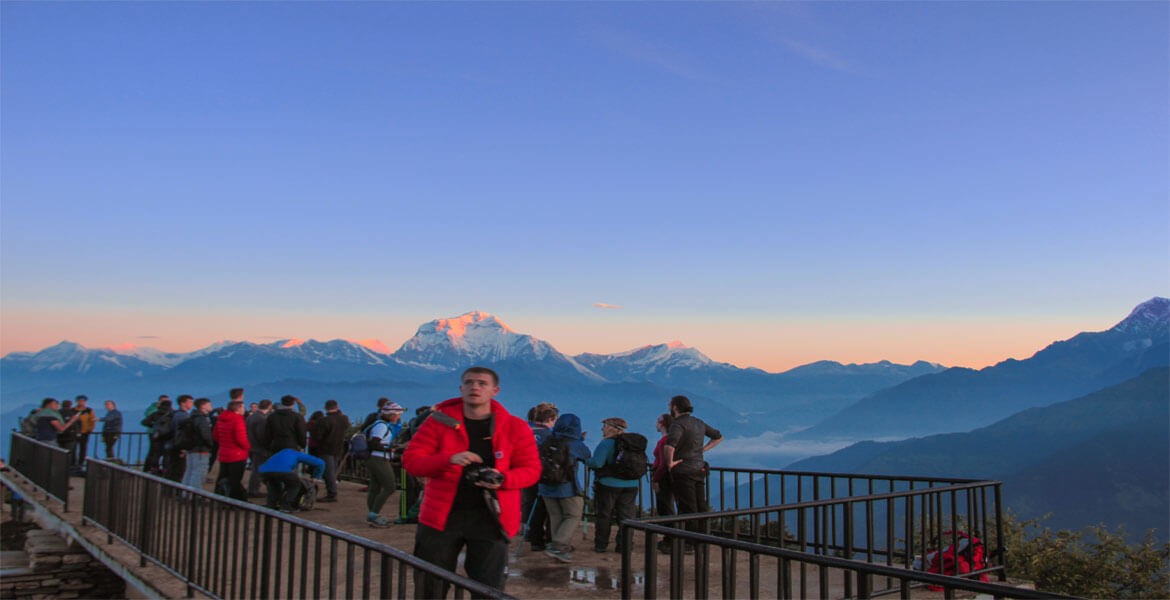 trekkers waiting sunrise at poon hill wearing warm equipment, morning mountain views with blue sky.