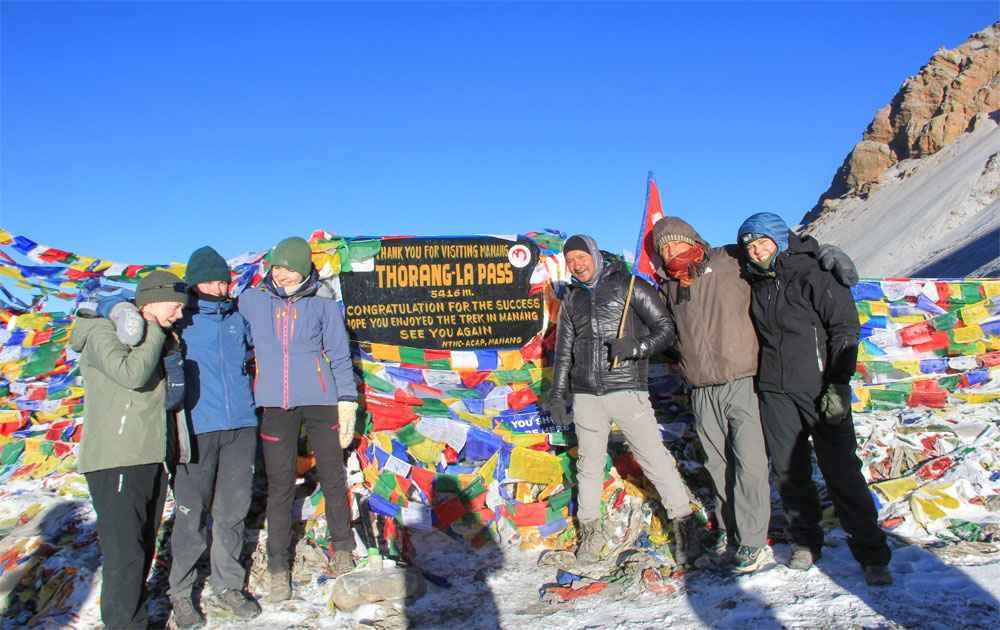 short annapurna circuit trekkers at thorong la pass, buddhist prayer flags on the top, and the blue sky on a clear day.